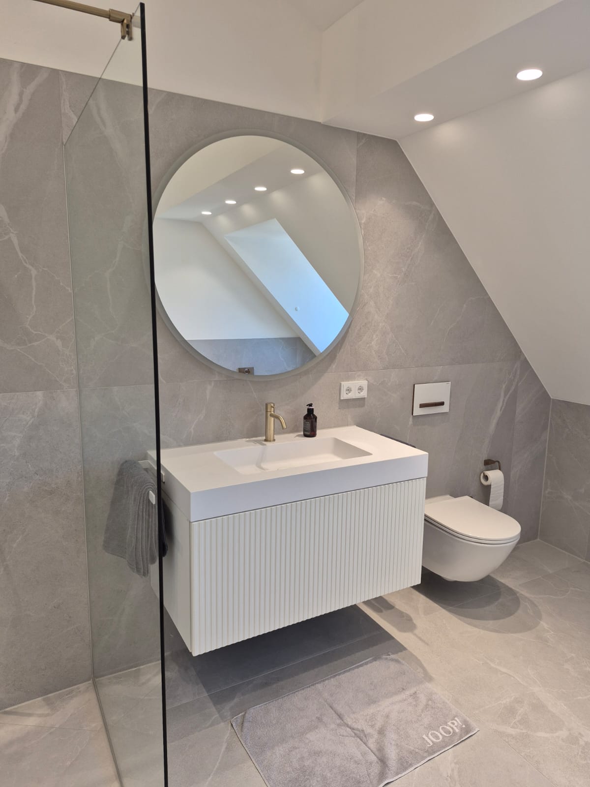 Modernisiertes Badezimmer mit Waschbecken und rundem Spiegel